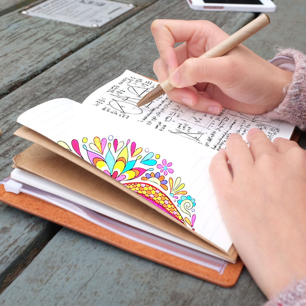 
A girl writing on midori style traveler's notebook with boho feathers design on a wooden table