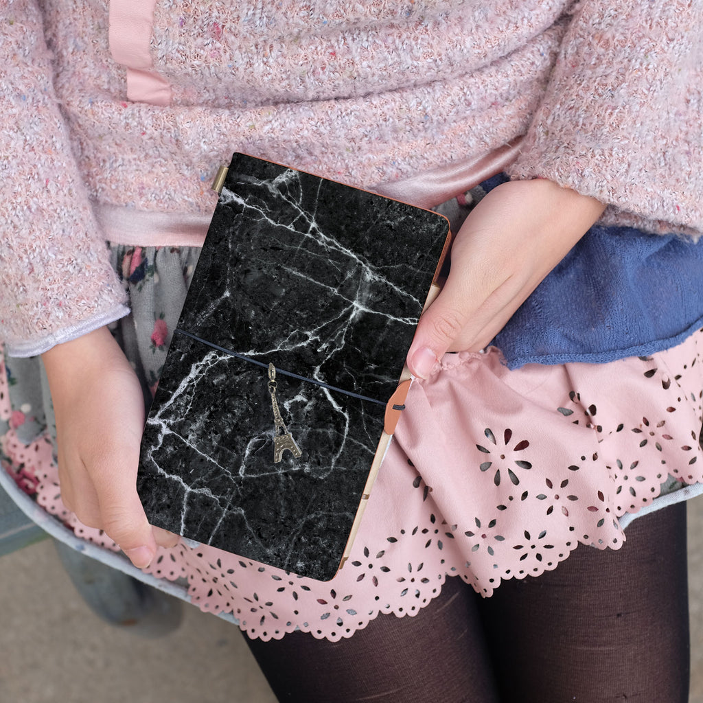 
a young girl showing midori style traveler's notebook with moody marble design above her leg